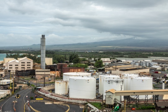 Kahului, Maui,, Hawaii, USA. - January 13, 2020: Big white fuel tanks and old sugarcane processing plant with chimney in the port area. Gray cloudscape with green mountain and fields in back.