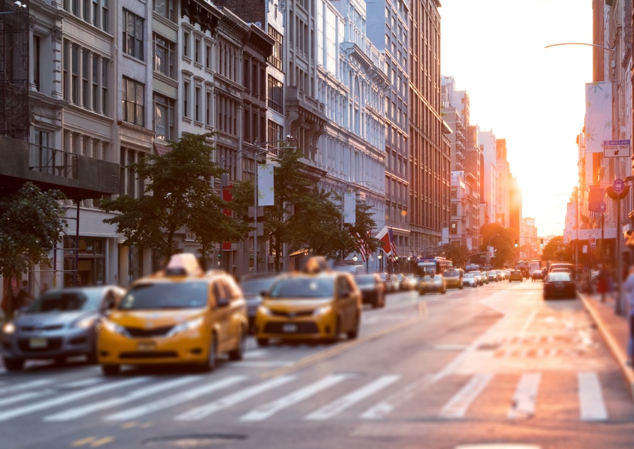 Sunlight shines down the streets of New York City with taxis stopped at the intersection