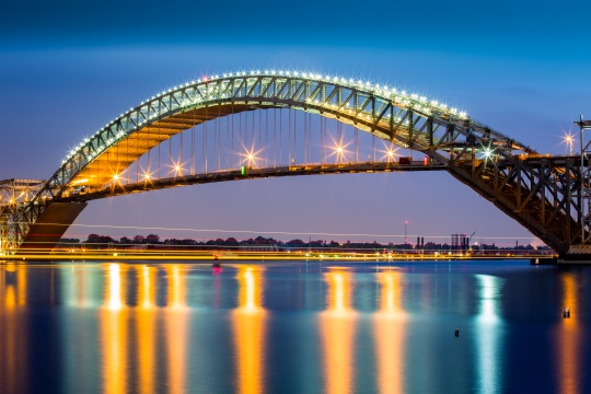 Bayonne Bridge at dusk. The Bayonne Bridge, is the 5th longest steel arch bridge in the world, spans the Kill Van Kull and connects Bayonne, NJ with Staten Island, NY