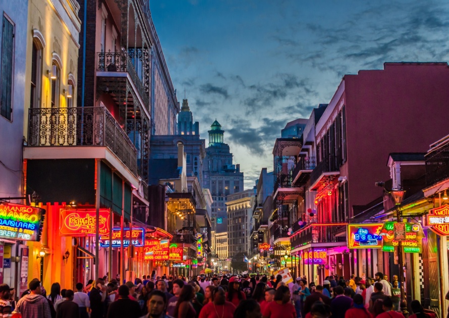 Tourist on Bourbon Street in New Orleans, Louisiana with illuminated signs at twilight.
