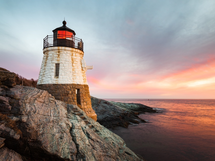 The small white Castle Hill Lighthouse is located on Newport's rocky shoreline on the island of Roda off the Atlantic coast of New England. Sunset with waves slowly rushing through the rocks.