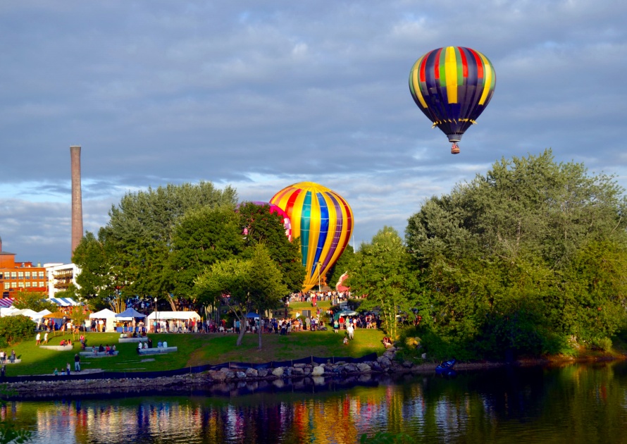 Lewiston-Auburn Maine`s Great Falls Annual Balloon Festival A vibrant colorful balloon takes flight against the beautiful blue sky. There is a colorful reflection in the water.