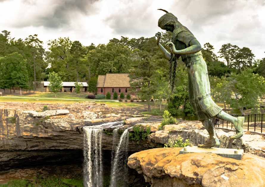 Gadsden, Alabama, USA - May 20, 2017: The nine-foot-tall bronze statue of Noccalula, a young Cherokee woman, who legend says plunged to her death at this point with Noccalula Falls in the background.